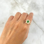 Hand wearing a ring with a green gemstone on a white marble background