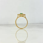 Gold ring with a green gemstone on a reflective surface with a light gray background