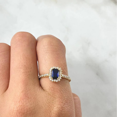 Ring with a blue gemstone on a finger against a neutral background