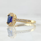 Gold ring with a blue gemstone and diamond accents on a reflective surface.