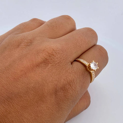 Gold ring with a diamond on a person's finger against a light gray background
