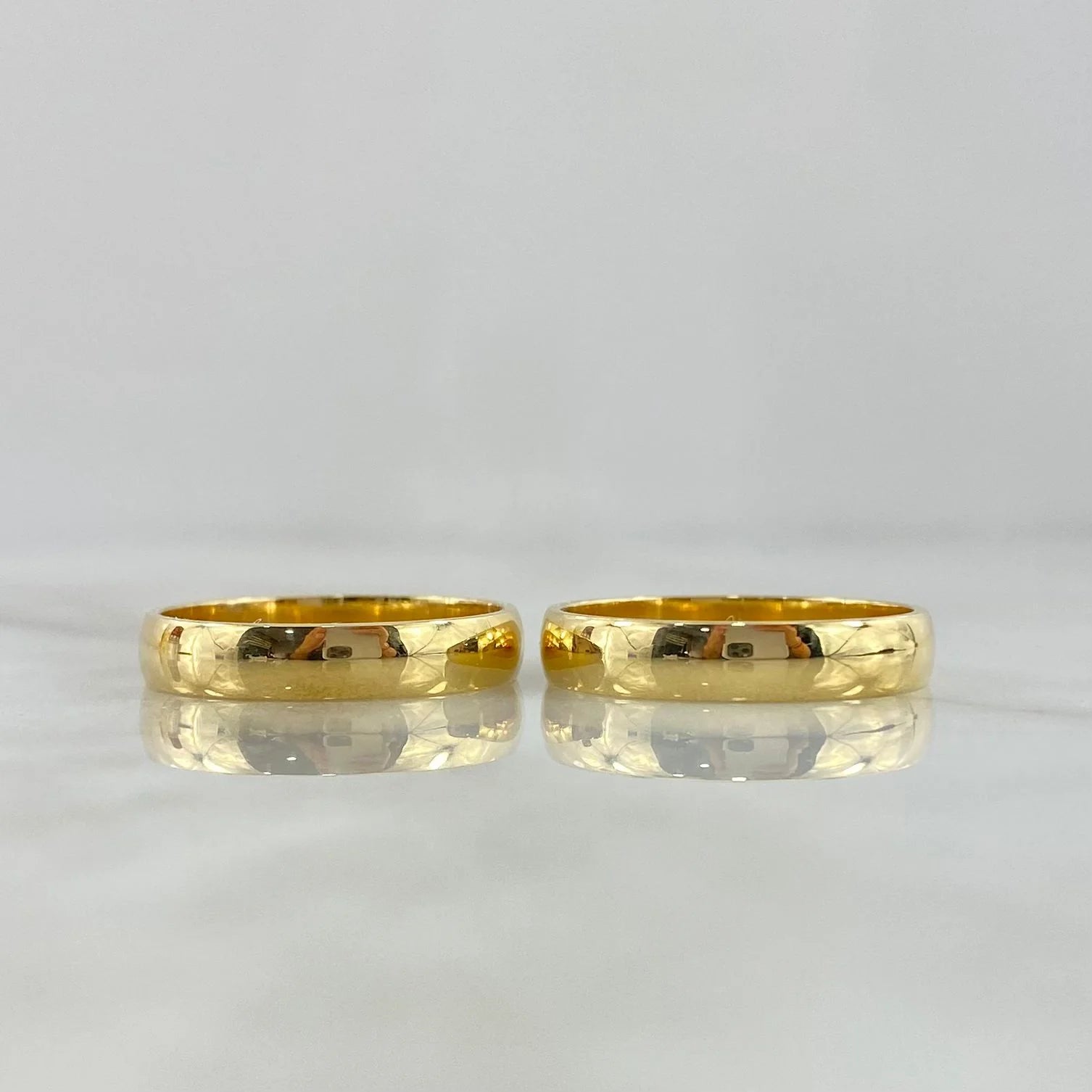 Two polished 18K gold wedding bands with a rounded profile and seamless continuous form.