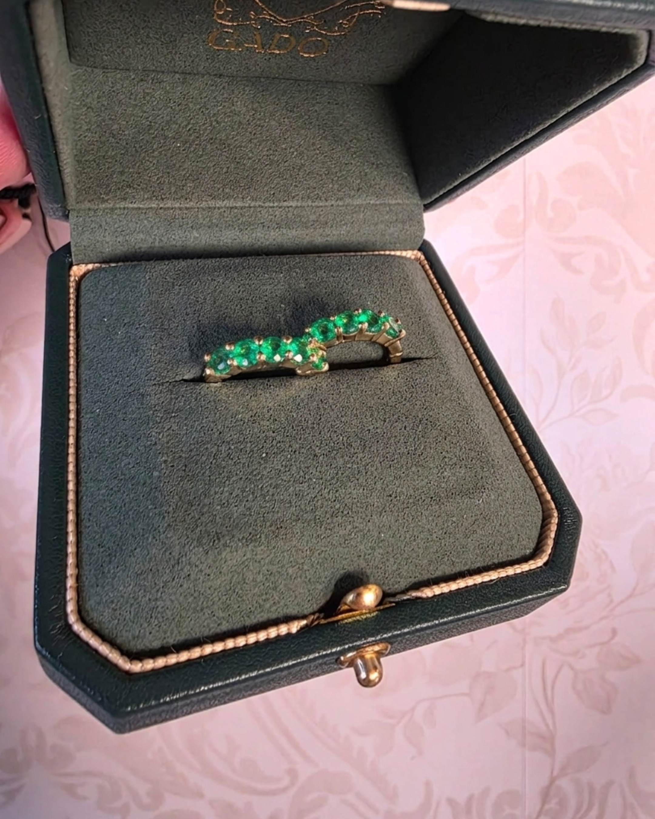 Green gemstone ring in a jewelry box on a pink textured background