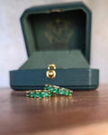 Gold ring with green gemstones on a wooden surface next to a green jewelry box.