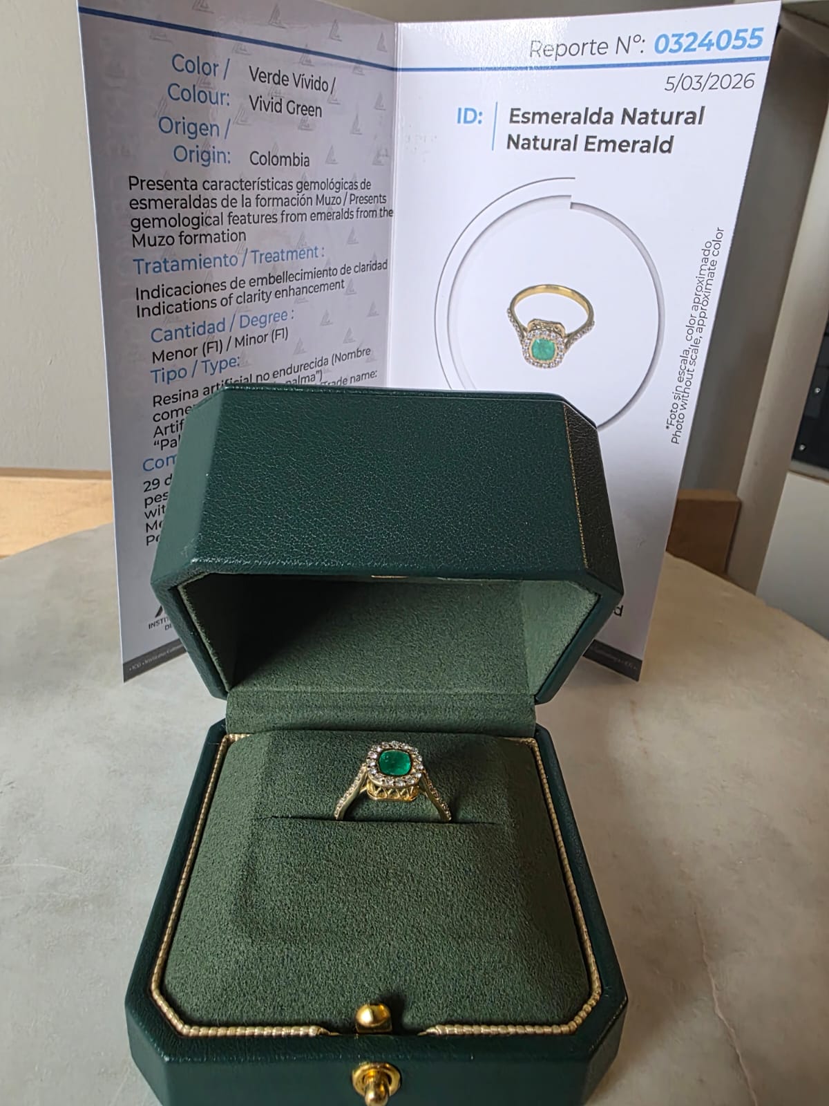 Gold ring with emerald in a green box, with a certificate in the background.