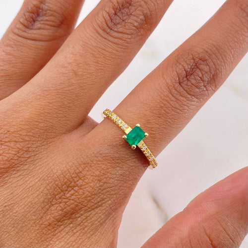 Gold ring with a green gemstone on a person's finger against a white background