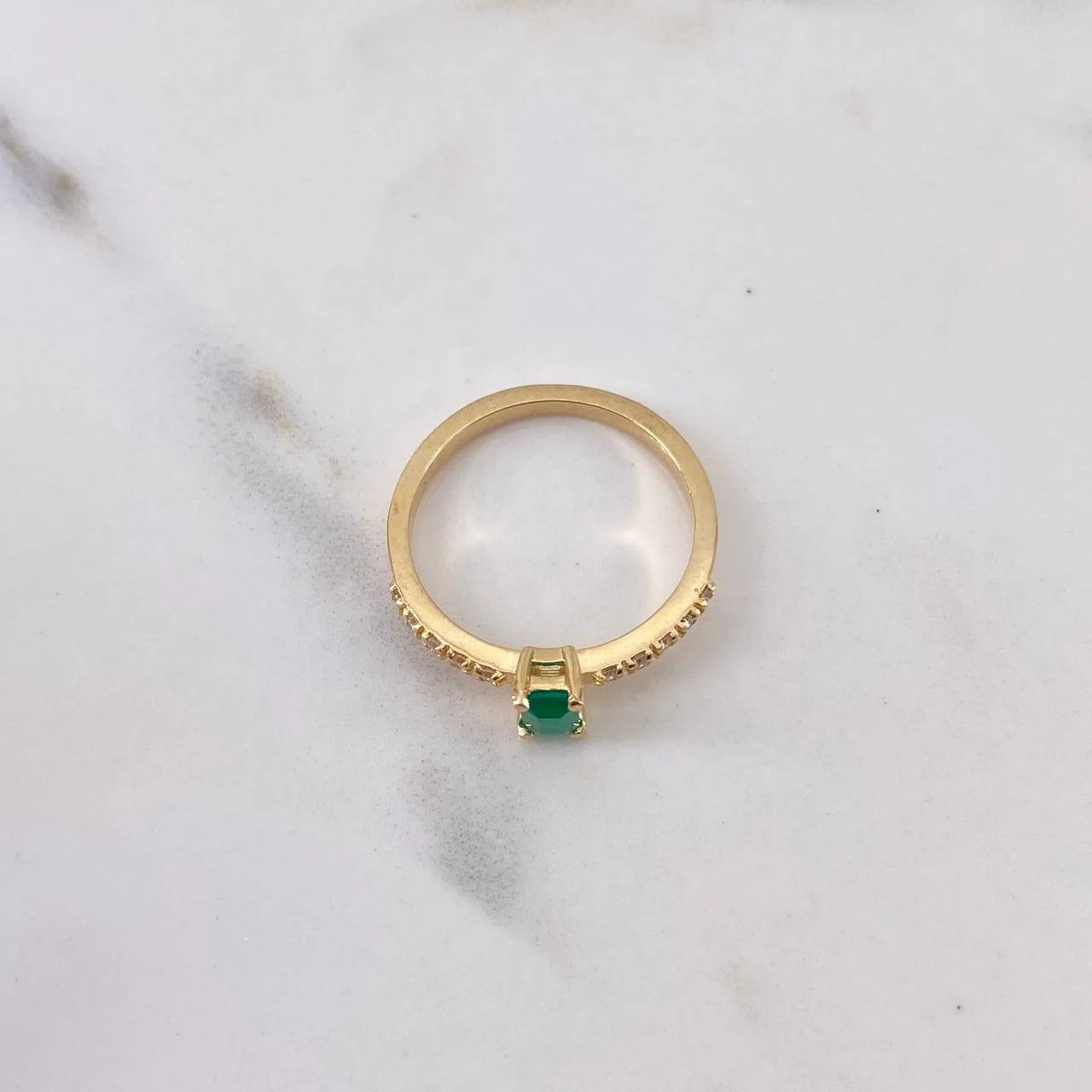 Gold ring with a green gemstone on a marble surface