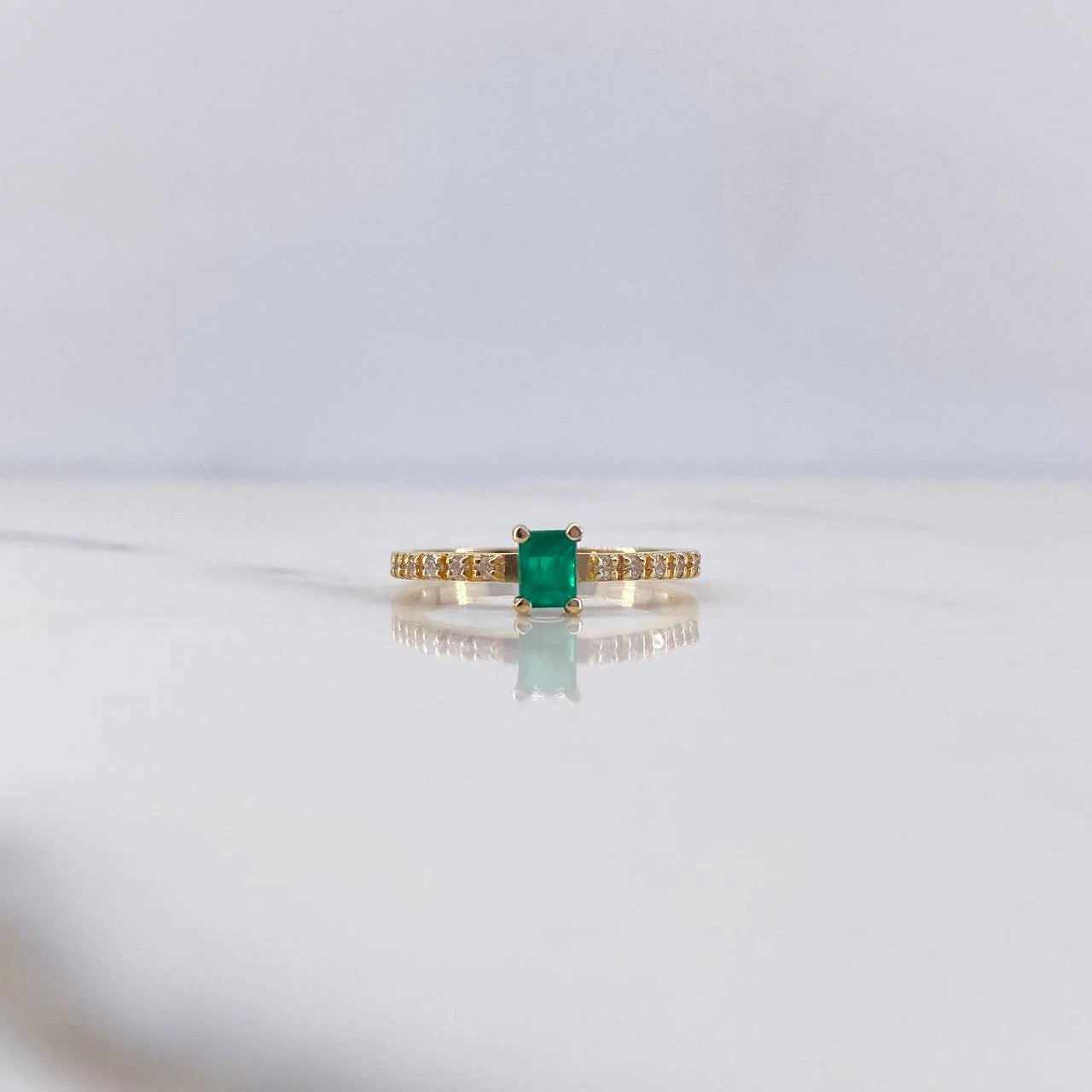 Gold ring with a green gemstone on a light gray background