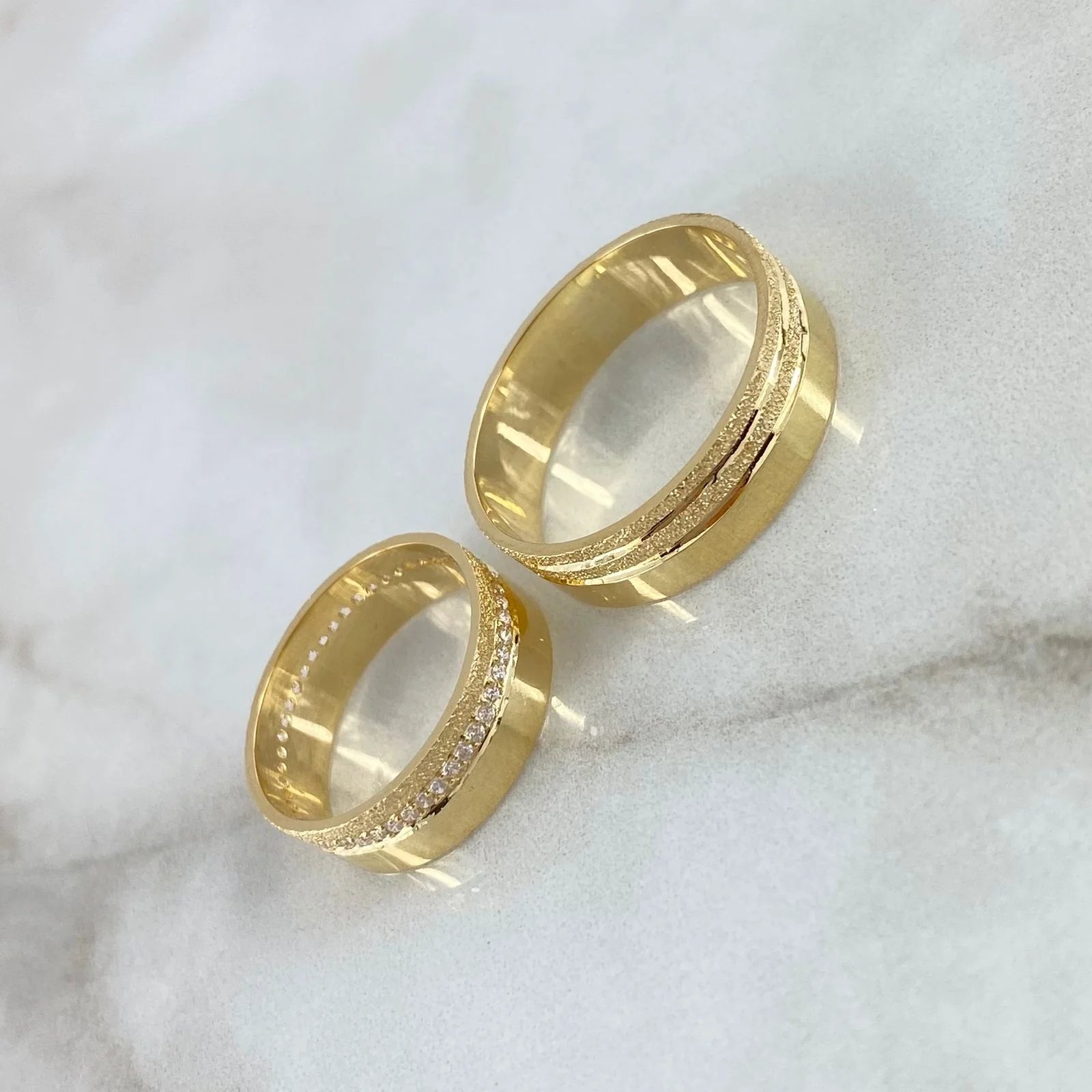 Two gold rings with diamond accents on a marble surface