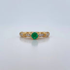 Gold ring with a green gemstone and diamond accents on a light gray background