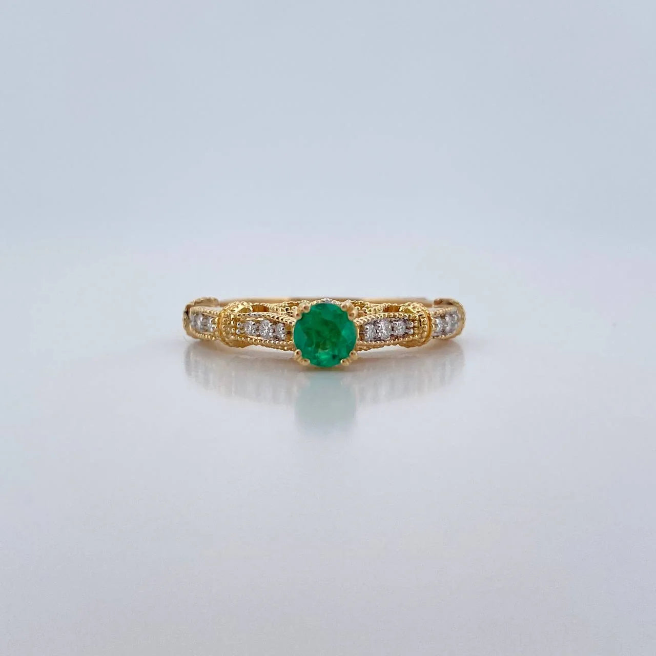 Gold ring with a green gemstone and diamond accents on a light gray background