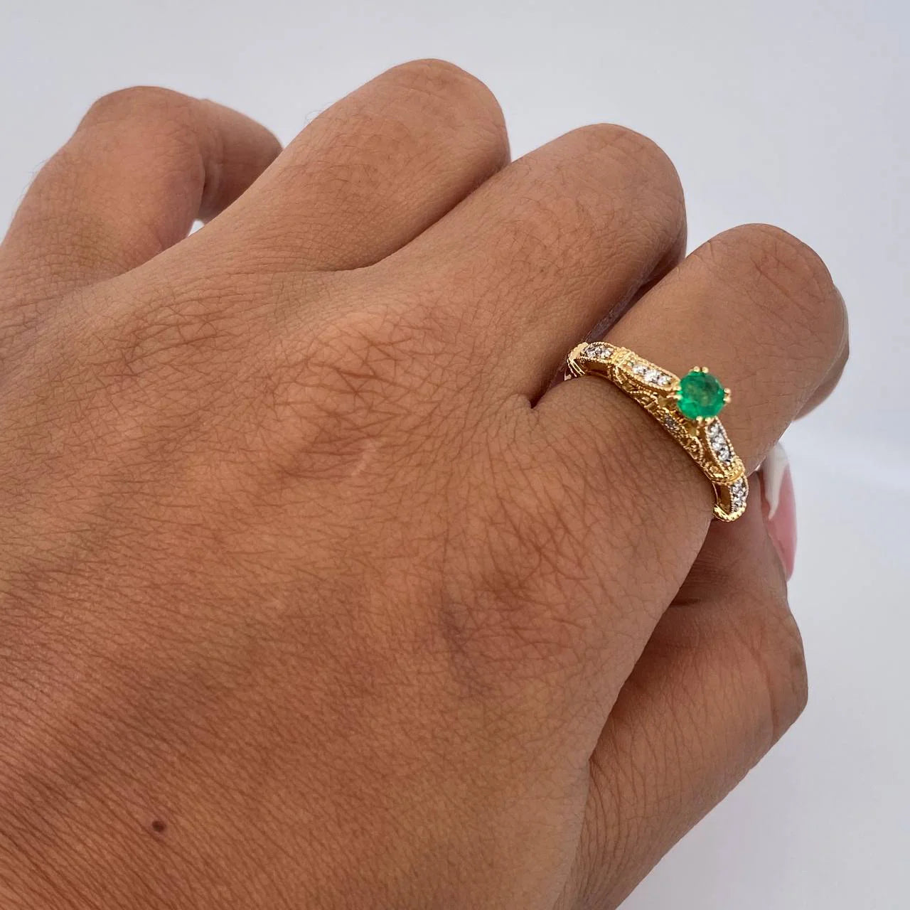 Gold ring with a green gemstone on a person's finger against a white background