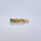 Gold ring with a green gemstone and diamonds on a light gray background