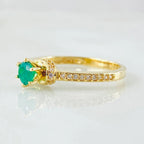 Gold ring with a green gemstone and small diamonds on a light gray background