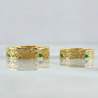 Two gold rings with green gemstones on a light gray background