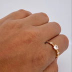Gold ring with a clear gemstone on a person's finger against a plain background