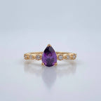 Gold ring with a purple gemstone on a light gray background