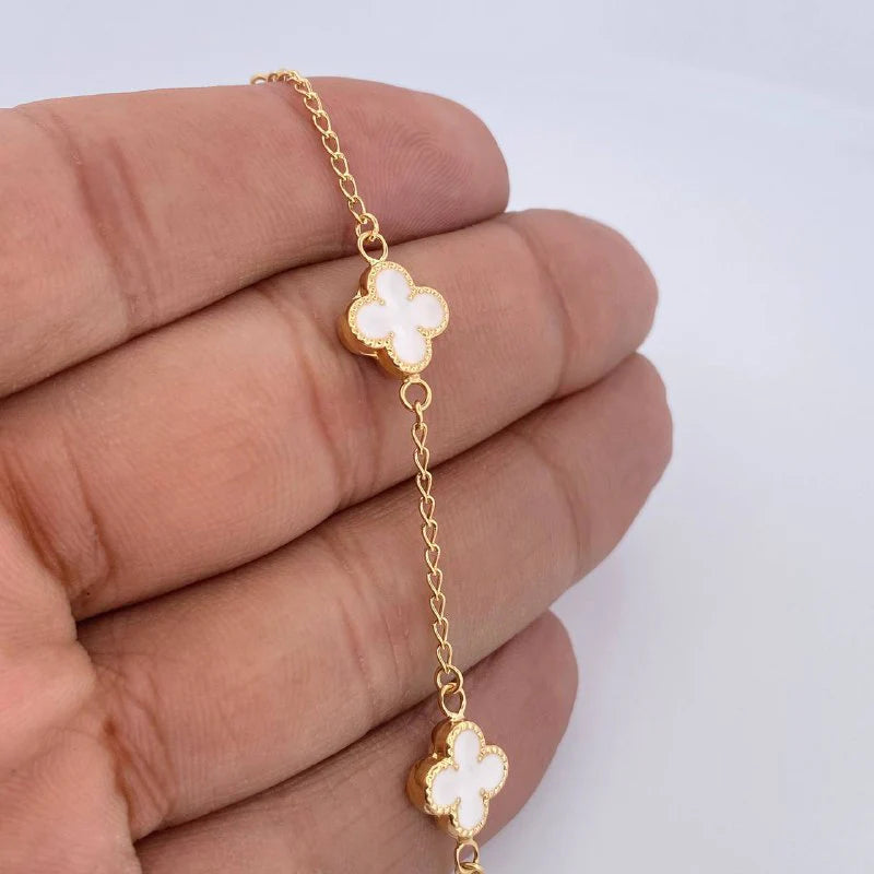 Gold necklace with clover-shaped pendants held between fingers on a light background