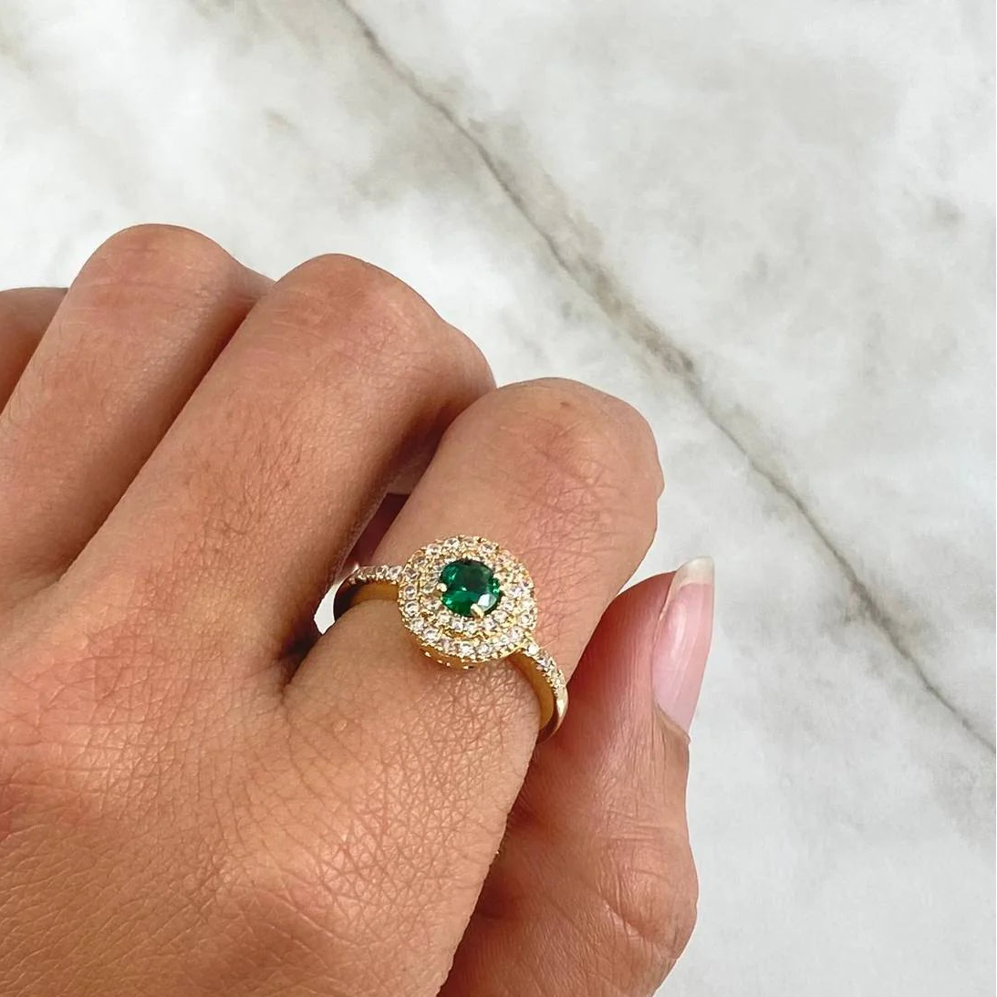 Hand wearing a gold ring with a green gemstone on a marble surface