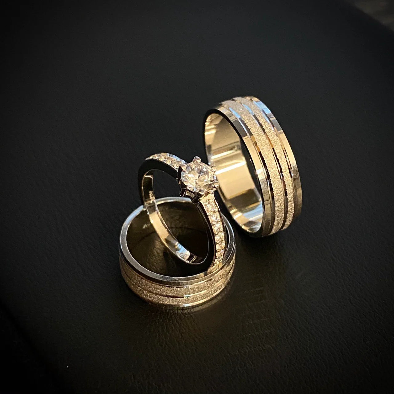 Three-piece white gold bridal set featuring a round diamond engagement ring with pavé shoulders, paired with two layered channel wedding bands in 18K gold