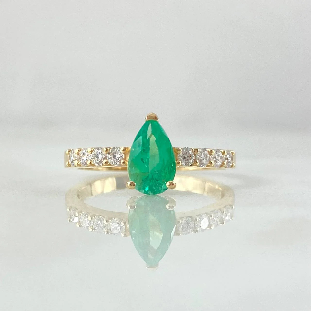 Gold ring with a green teardrop gemstone and diamond accents on a light gray background