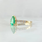Gold ring with a green gemstone and diamond accents on a light gray background