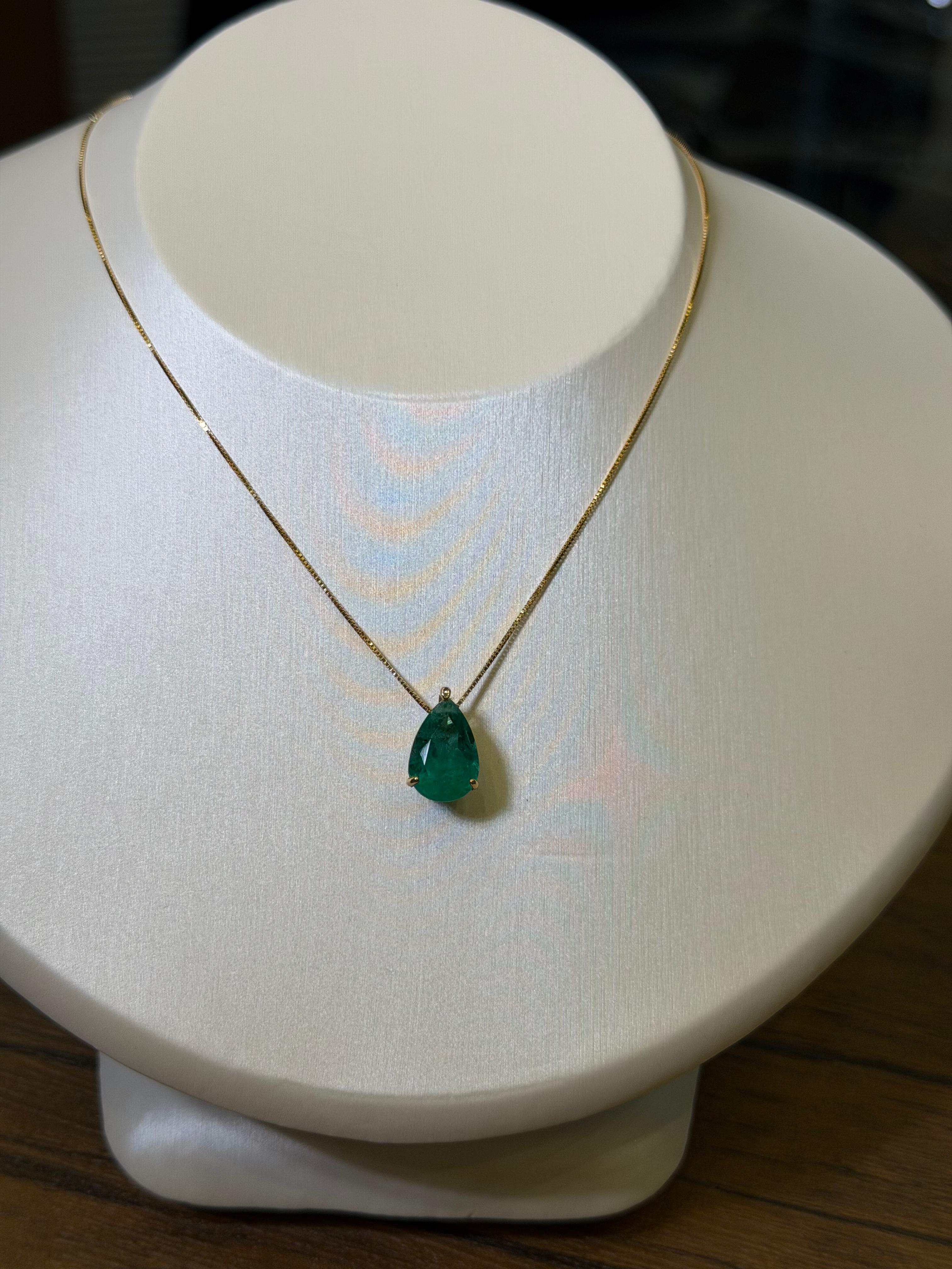 Emerald teardrop pendant on a gold chain displayed on a mannequin bust.