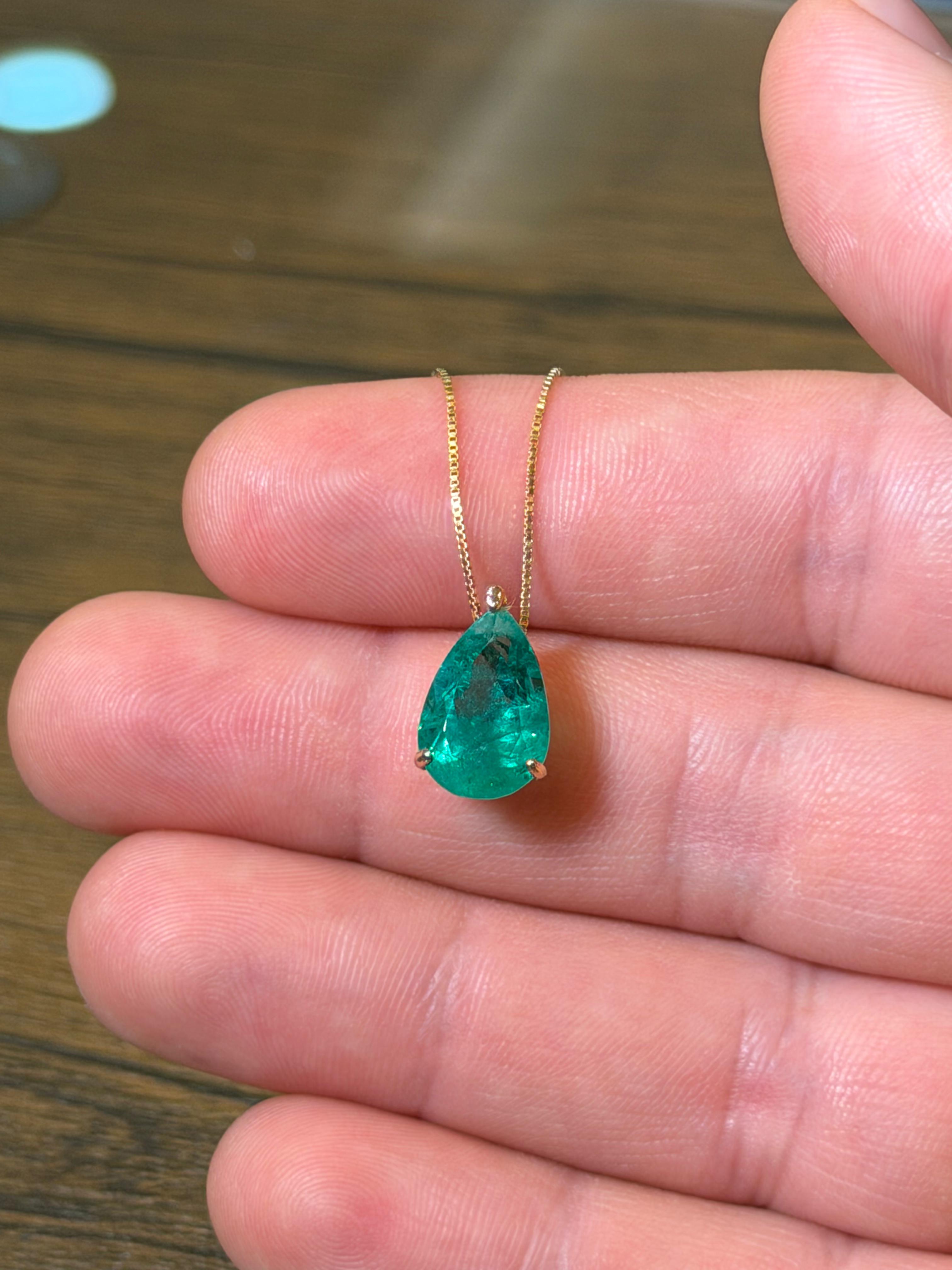 Green teardrop pendant on a gold chain held between fingers against a wooden surface