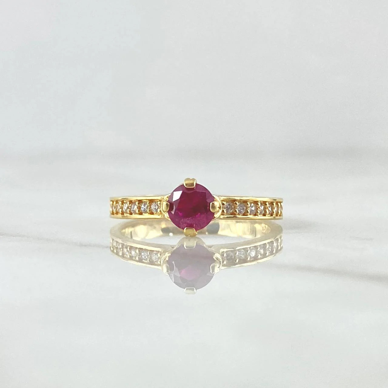 Gold ring with a red gemstone on a light gray background