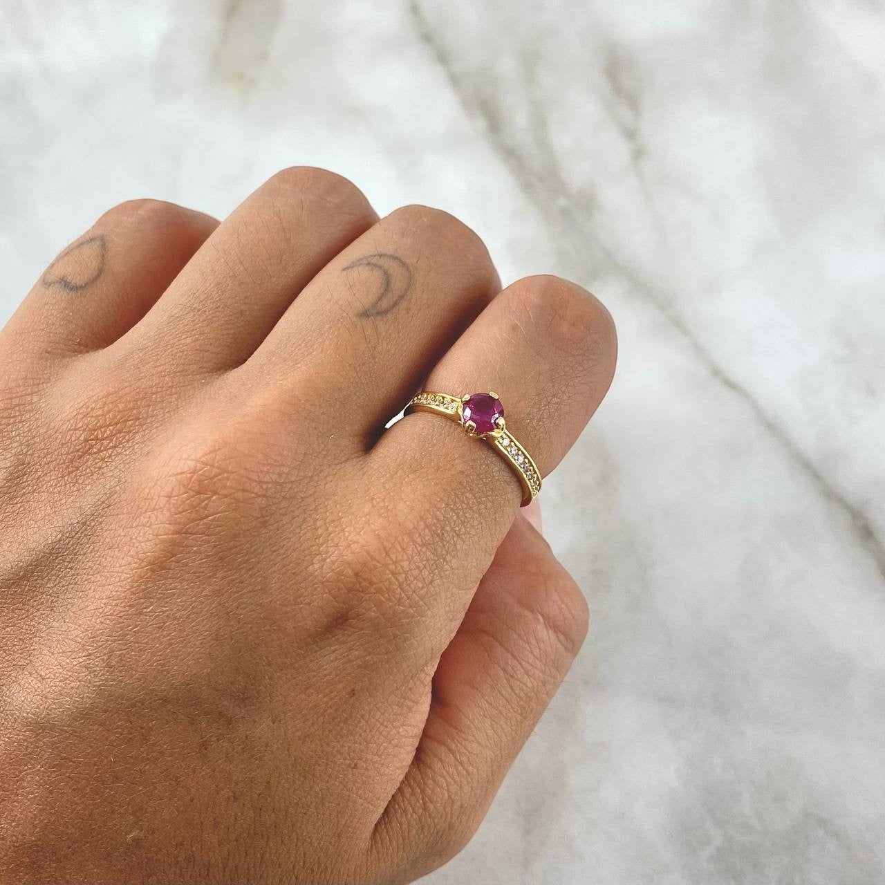 Hand wearing a gold ring with a purple gemstone on a white background
