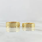 Two structured 18K gold wedding bands with a brushed central channel and polished edge framing.