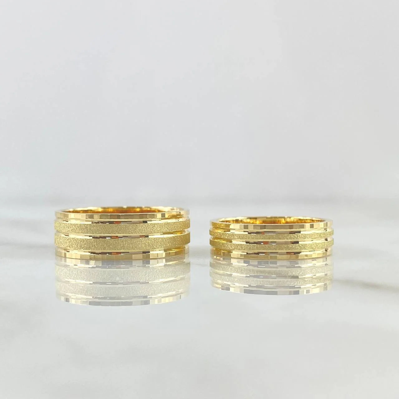 Two structured 18K gold wedding bands with a brushed central channel and polished edge framing.