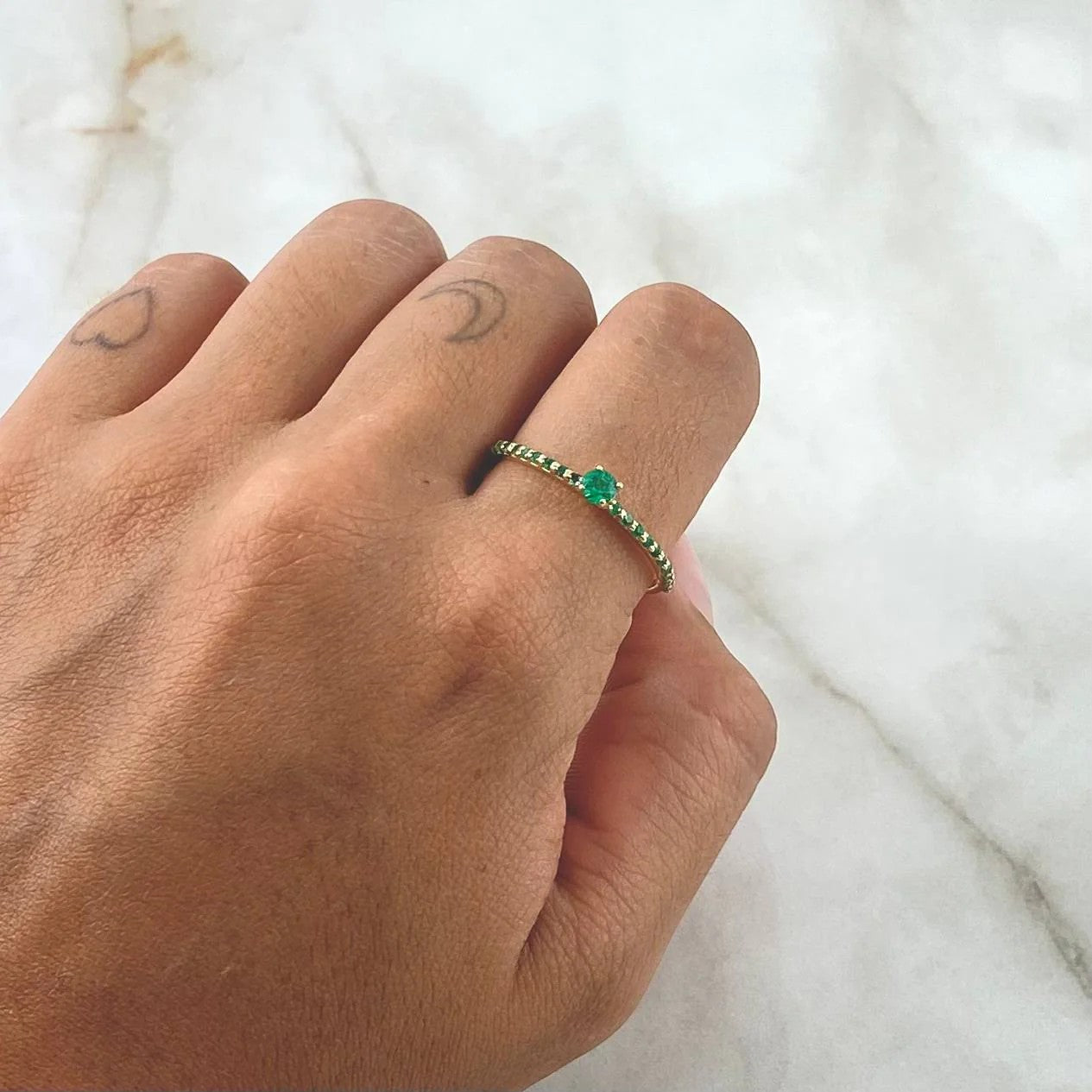 Hand wearing a green gemstone ring on a marble surface