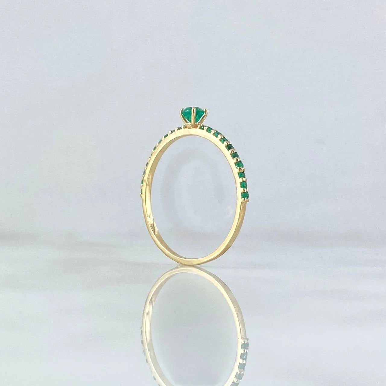 Gold ring with green gemstones on a light gray background