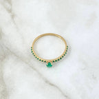 Gold ring with green gemstones on a white marble surface