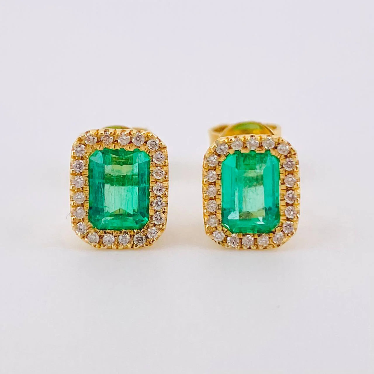 Pair of emerald green gemstone earrings with gold and diamond accents on a white background