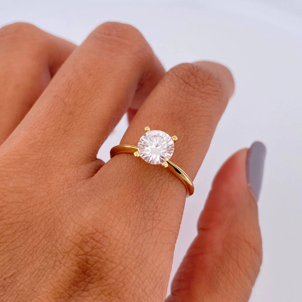 Gold ring with a diamond on a person's finger against a white background