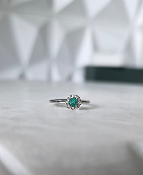 Round-cut Colombian emerald and diamond halo ring in 18K white gold by Gado Jewellers