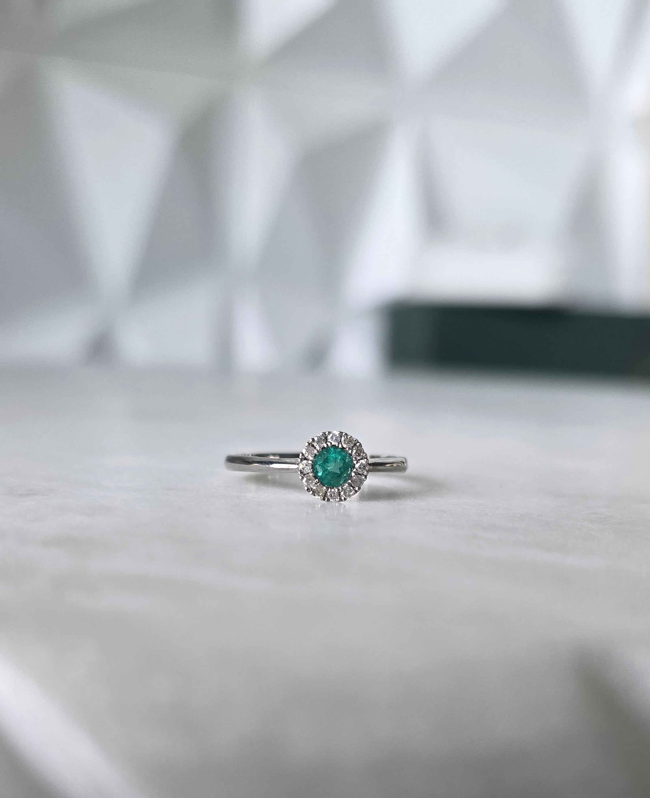 Round-cut Colombian emerald and diamond halo ring in 18K white gold by Gado Jewellers