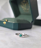 Round-cut Colombian emerald and diamond halo ring in 18K white gold by Gado Jewellers
