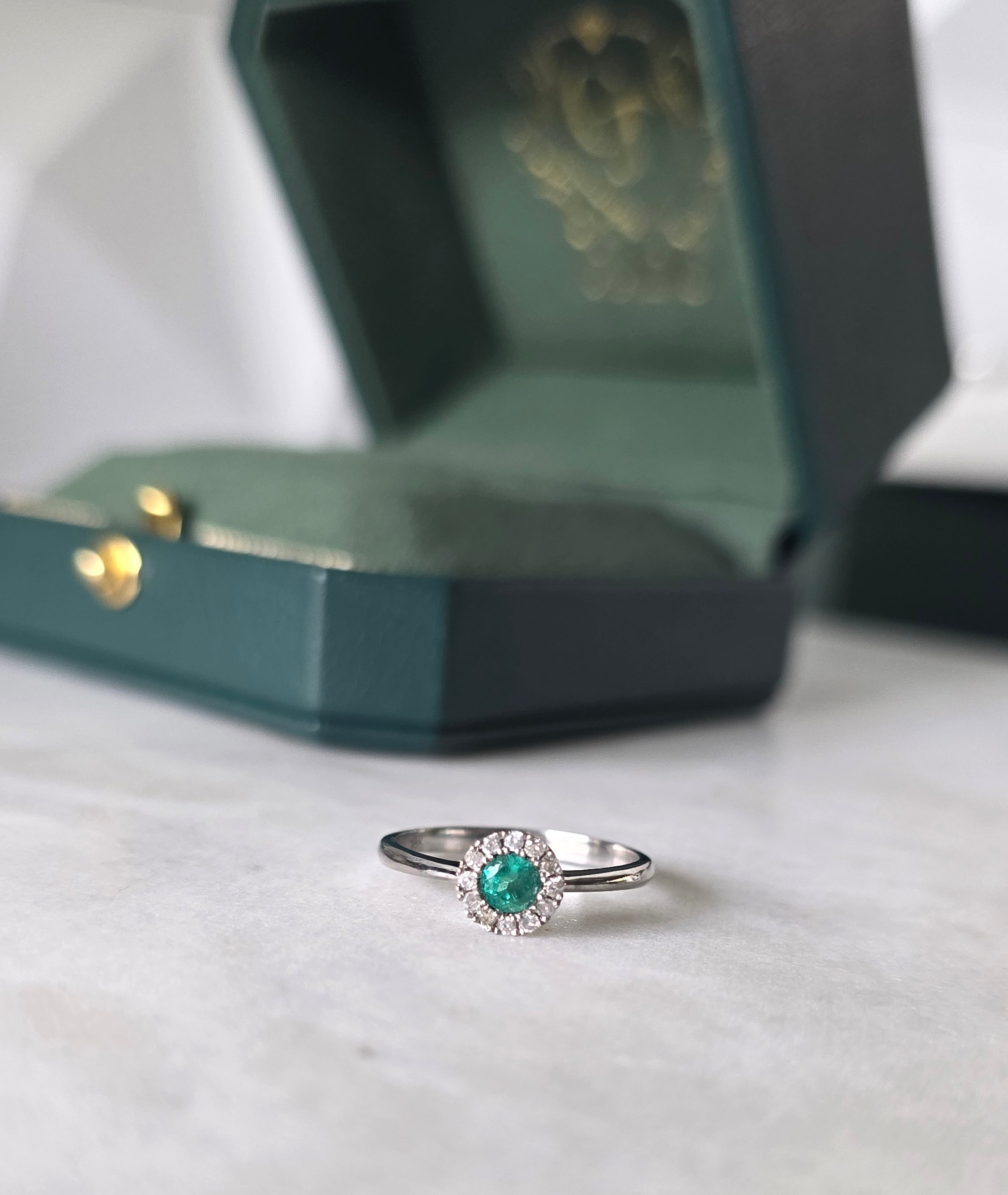 Round-cut Colombian emerald and diamond halo ring in 18K white gold by Gado Jewellers