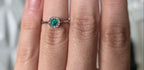 Colombian emerald diamond halo ring worn on hand, 18K white gold, Gado Jewellers