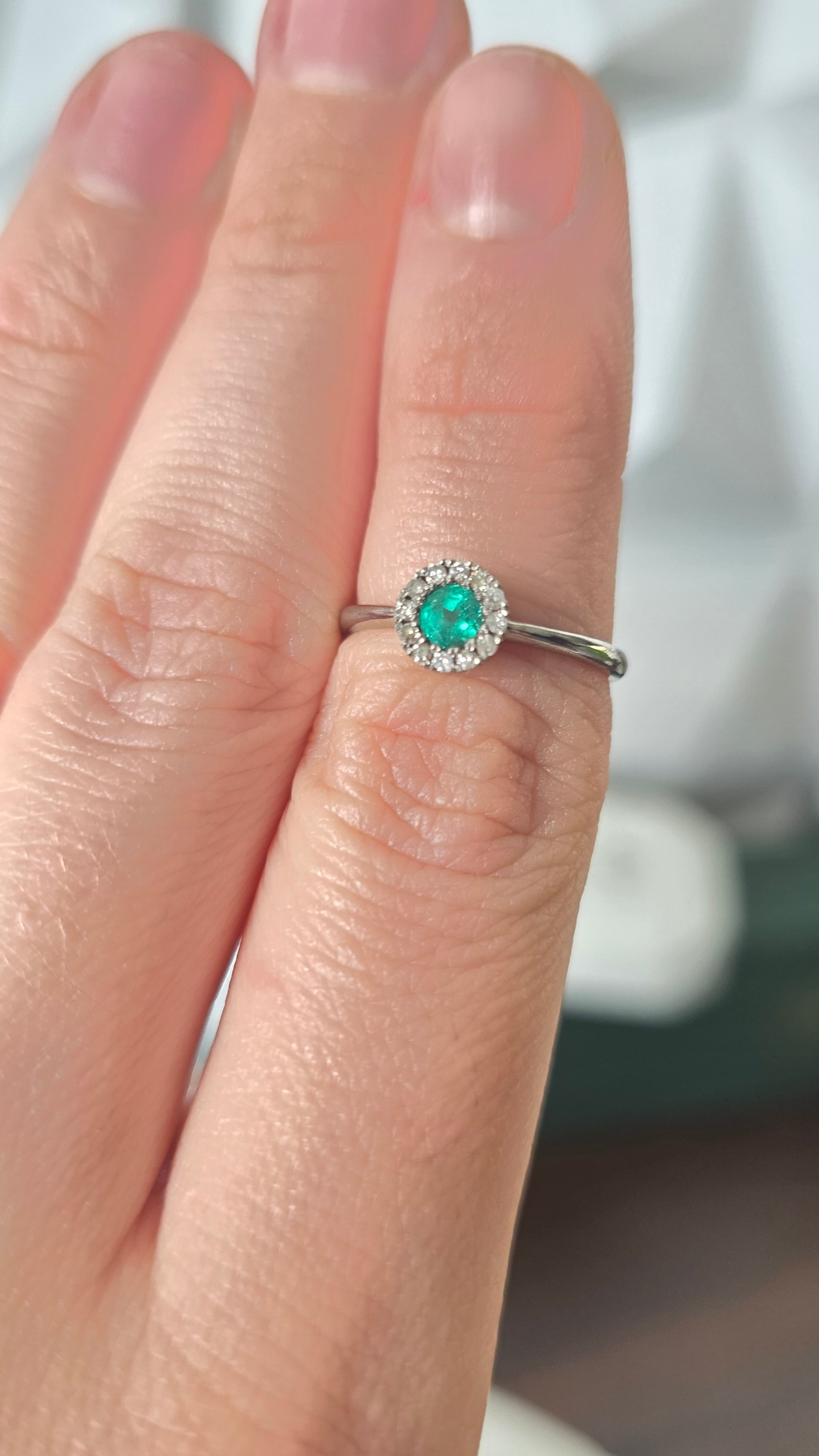 Colombian emerald diamond halo ring worn on hand, 18K white gold, Gado Jewellers