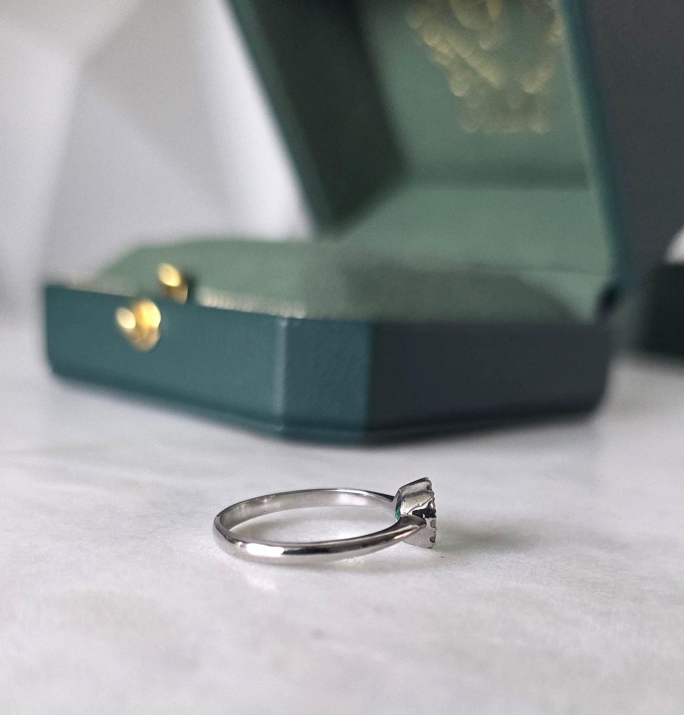 Side profile of Colombian emerald diamond halo ring in 18K white gold by Gado Jewellers