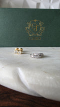 Two diamond earrings on a white surface with a green jewelry box featuring a gold logo.